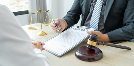 Lawyer hand holding pen and providing legal consult business dispute service at the office with justice scale and gavel hammer.の写真素材