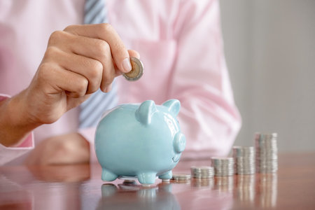 Businessman hand putting coin into blue piggy bank, step up start up business to success, Saving money for future plan and retirement fund conceptの写真素材