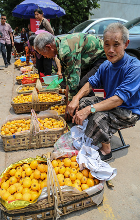  old farmers selling loquat in the market in chengdu,chinaのeditorial素材