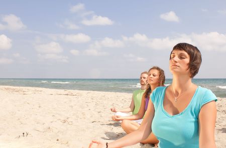 three young people meditating on the beachの写真素材