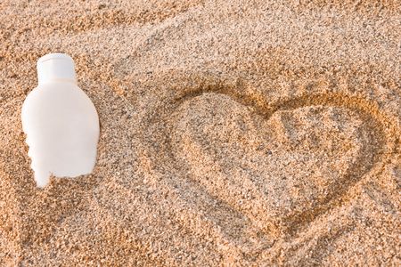 bottle of sun lotion lies in the sand beside a hartの写真素材