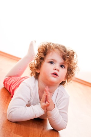 cute little girl with blond curly hair lying posing on floorの写真素材