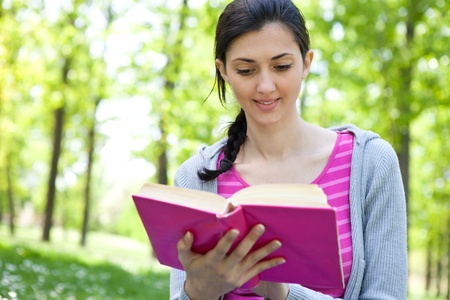 young girl studying in nature, smiling and  holding  book の写真素材