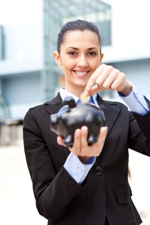 businesswoman putting coins money in piggy bank in front her office buildingの写真素材