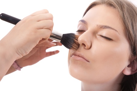 make-up artist applying powder on face of young model, isolated on white