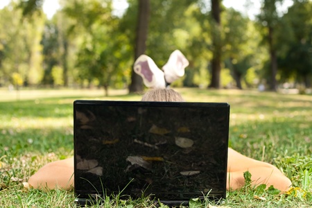 Young woman lying on grass in park behind laptopの写真素材