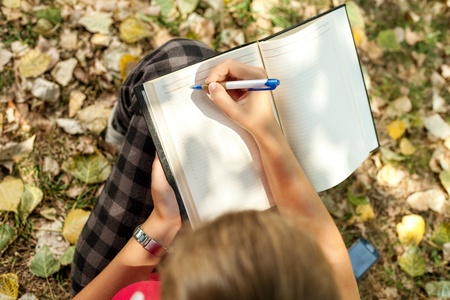 girl sitting outdoor and writing , top view