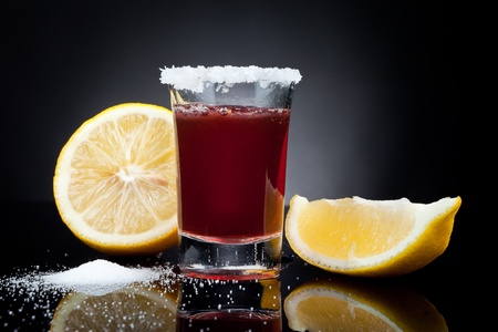 Shot glass full of dark colored alcohol  with a lemon on black backgroundの写真素材