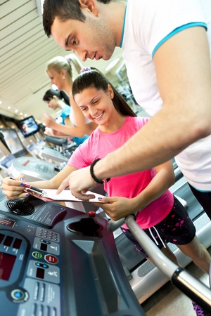 young man with instruction checking his results in gym 