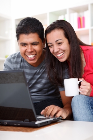 Laughing young couple looking at laptop in homeの写真素材