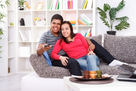 Smiling young couple watching TV on couch at home の写真素材