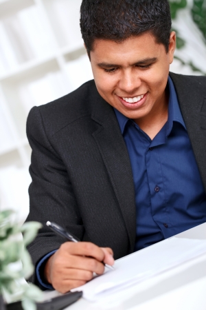 Smiling businessman taking notes at office desk , hand with pen in focusの写真素材