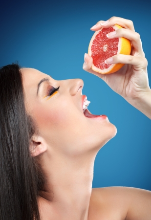 Young beautiful woman squeezing orange into mouth, sensual refreshmentの写真素材