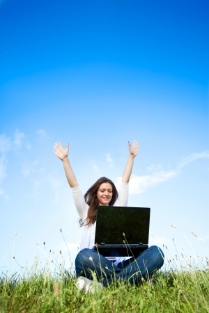 Happy girl with laptop sitting on grassの写真素材