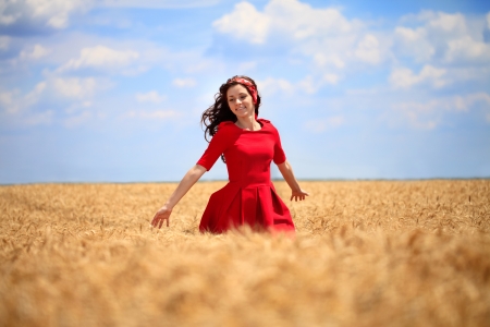 
beautiful girl in a red dress walking through a wheat field.の写真素材