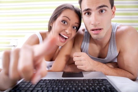 
funny young couple with laptop looking at camera as screenの写真素材