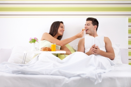 beautiful couple having breakfast in bed, girl feeding her boyfriendの写真素材