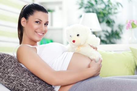 
Smiling pregnant woman lying on couch with teddy bearの写真素材