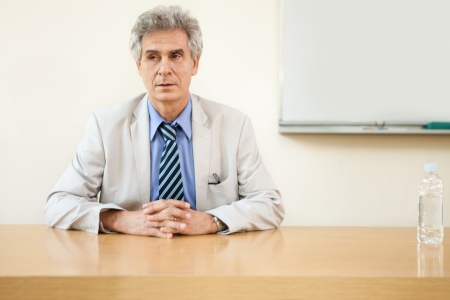 Portrait of confident senior male professor sitting at deskの写真素材