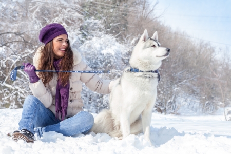 young beautiful woman sits with husky dog in the winter forestの写真素材