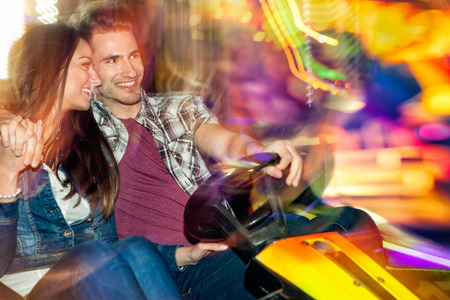 Young couple in love in a bumper car / dodgem ride, having fun in amusement parkの写真素材