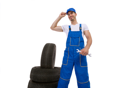 Young mechanic standing with car tires and holding a wrenchの写真素材