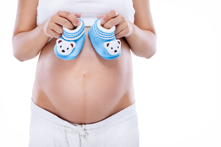 Pregnant woman holding on her naked belly pair of baby shoes