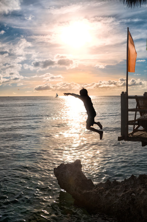 Silhouettes of child jumping in sea over sunsetの写真素材
