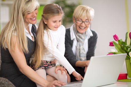 Little girl using laptop with mother and grandmother, modern technology for all generations