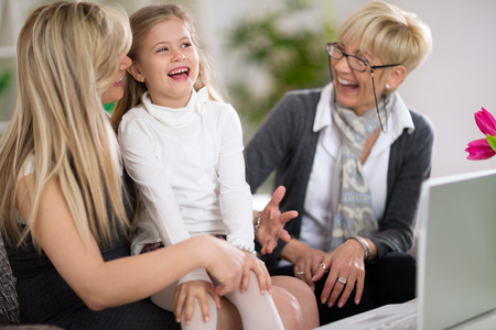 Laughing little girl with mother and grandmother using laptop