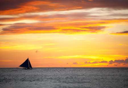 Sailing boat over beautiful orange sunsetの写真素材