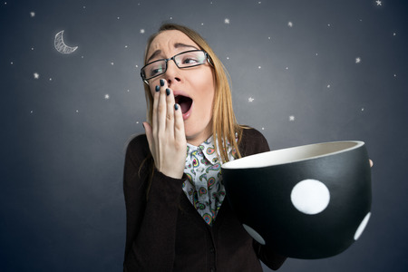 tired female student yawning with big cup of coffeeの写真素材