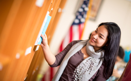 Beautiful young Asian student choosing book in libraryの写真素材