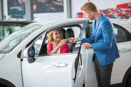 Happy woman buying a new car and salesman handling keysの写真素材