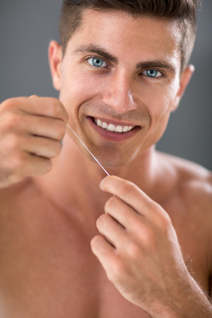 handsome young shirtless man cleaning his teeth with dental floss and smiling while standing in front of the mirror.の写真素材