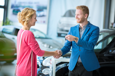 Happy woman  getting car keys from a car sellerの写真素材