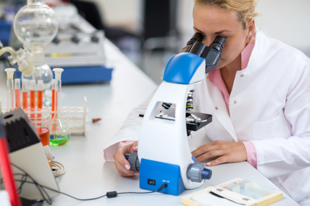 Female chemical technician  exam sample with microscopeの写真素材