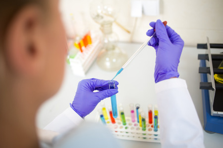 Close up view of lab technician sampling colorful liquids with glass pipette
