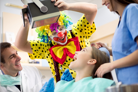 Funny clown in colorful clown suit make laugh young girl in dental ambulanceの写真素材