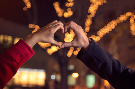 couple making heart shape with hands over the Christmas illuminationの写真素材