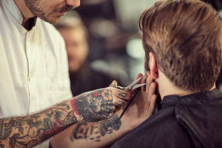 close up hairdresser with scissors cut the beard of clientの写真素材