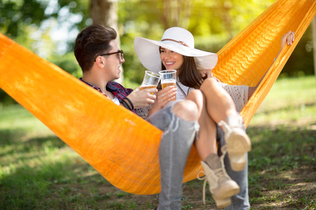 Lovely lassie with boyfriend toast with glasses of beer in hammock in forestの写真素材