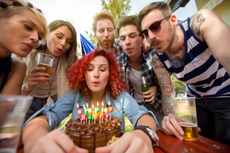 Birthday girl blows candles on chocolate birthday cake with friendsの写真素材