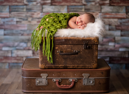 Little newborn baby peacefully sleeping on rustic  suitcases, travel or newborn photography concept