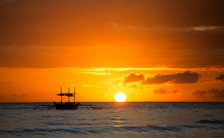 Sailboat sunset fantasy with a silhouetted boat sailing along against a vivid colorful sunset orange and yellow color filled sky.の写真素材