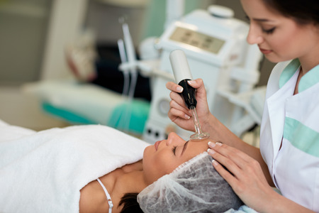 Professional cosmetologist undergoing darsonvalization on skin of face, skin and body care at beauty...