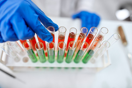 Scientist hand holding a laboratory glass test tube filled with red end green liquid