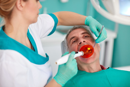 Female dentist with special lighting instrument repairing tooth to patient at clinicの写真素材