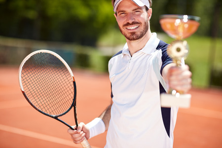 Male winner in tennis holding beaker and racketの写真素材
