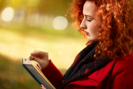 Profile of ginger female reading book outsideの写真素材